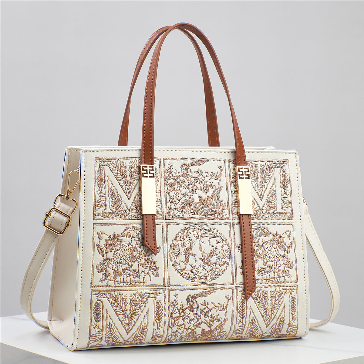 Designer handbag with intricate patterns and brown straps on a light gray background