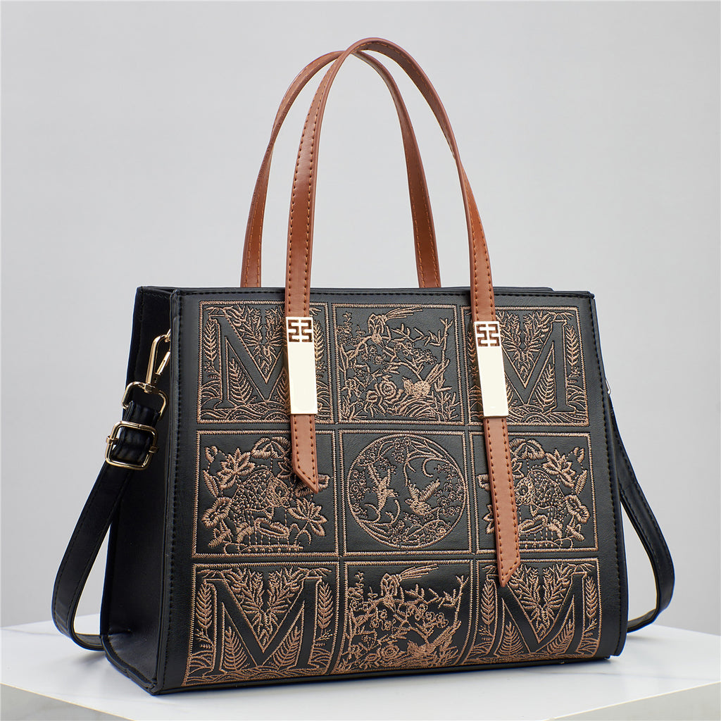 Black handbag with brown leather straps and intricate designs on a light gray background