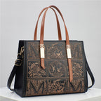 Black handbag with brown leather straps and intricate designs on a light gray background