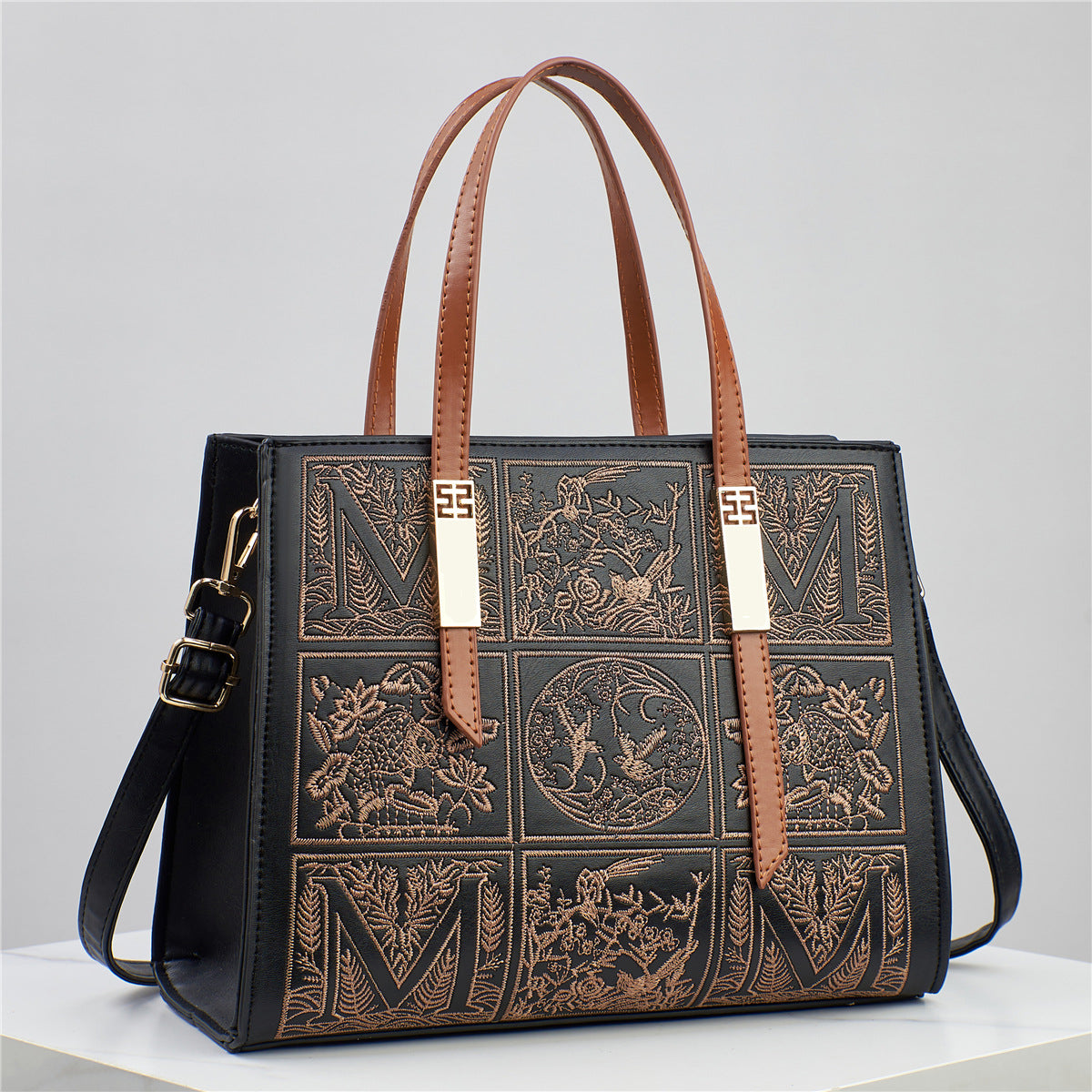 Black handbag with brown leather straps and intricate designs on a light gray background