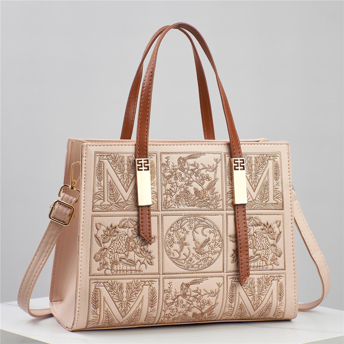 Designer handbag with intricate patterns and brown straps on a light gray background
