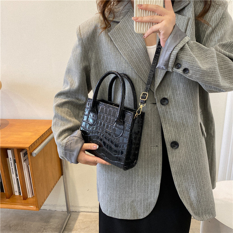 Person wearing a gray blazer holding a black handbag indoors.