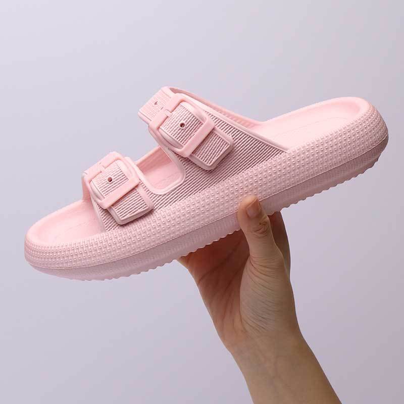 Pink slip-on shoe with buckles held against a light gray background