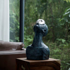 Decorative sculpture with a spherical object on top, placed on a wooden surface with a blurred natural background.