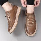 Brown leather shoes with beige soles worn by a person on a gray background