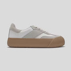 Sneaker with a white and gray upper and brown sole on a light gray background