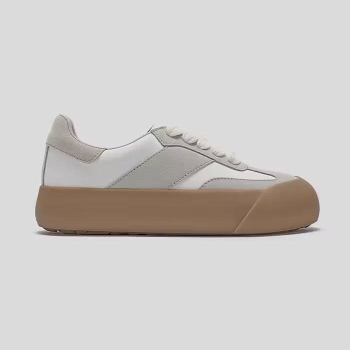 Sneaker with a white and gray upper and brown sole on a light gray background