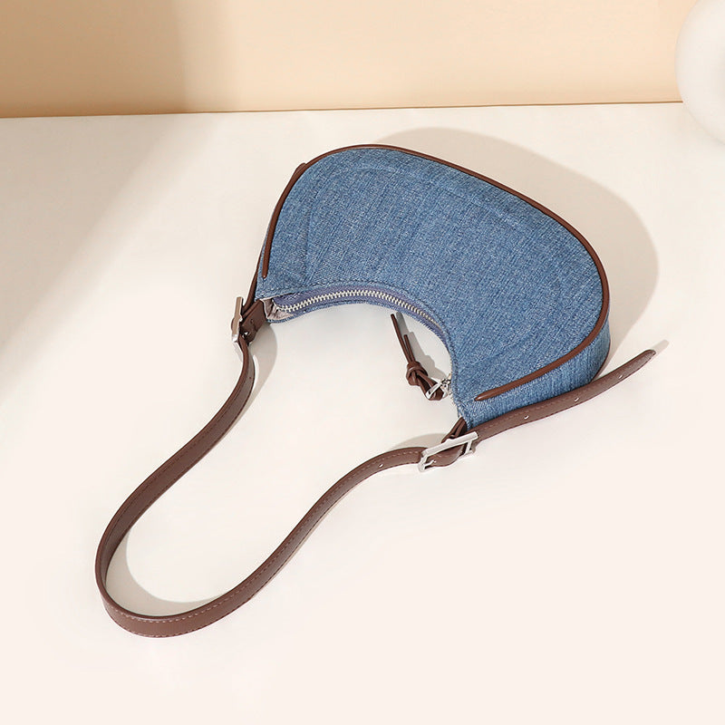 Blue denim pouch with brown leather strap on a white surface
