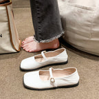 White shoes with buckles on a carpeted floor next to a white bag.