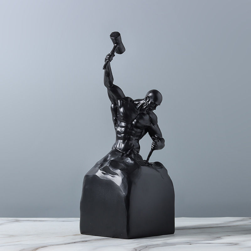 Black sculpture of a muscular figure on a marble surface with a gray background