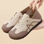 Beige and brown sneakers with a hand lifting one of them on a beige background