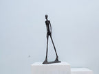Black abstract sculpture on a white pedestal against a light gray background