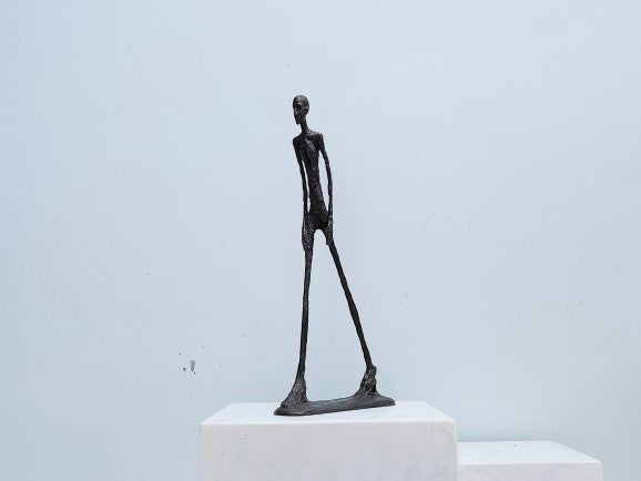 Black abstract sculpture on a white pedestal against a light gray background