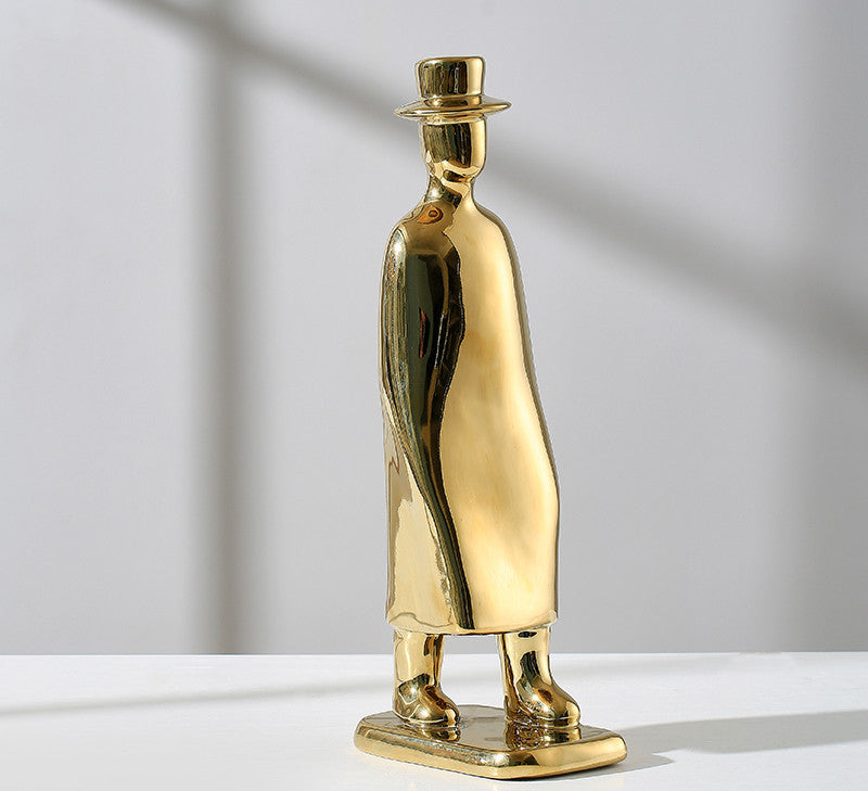 Gold-colored figurine of a person wearing a top hat on a white surface with a gray background
