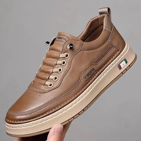 Brown leather shoe held by a hand against a gray background