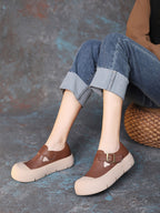 Brown platform shoes worn with rolled-up jeans on a textured surface