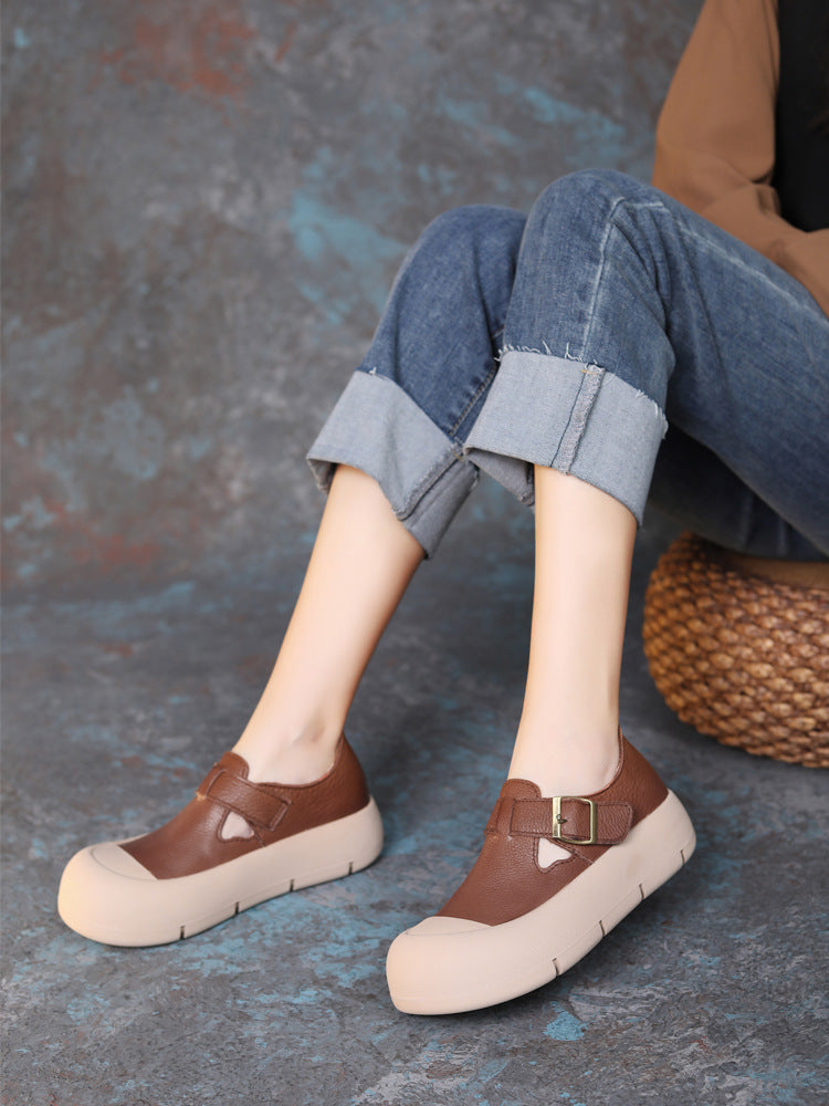 Brown platform shoes worn with rolled-up jeans on a textured surface