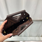 Brown leather clutch bag held by a hand against a white curtain background