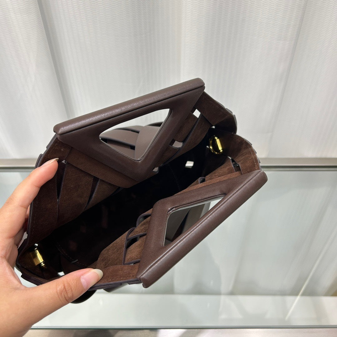 Brown leather clutch bag held by a hand against a white curtain background