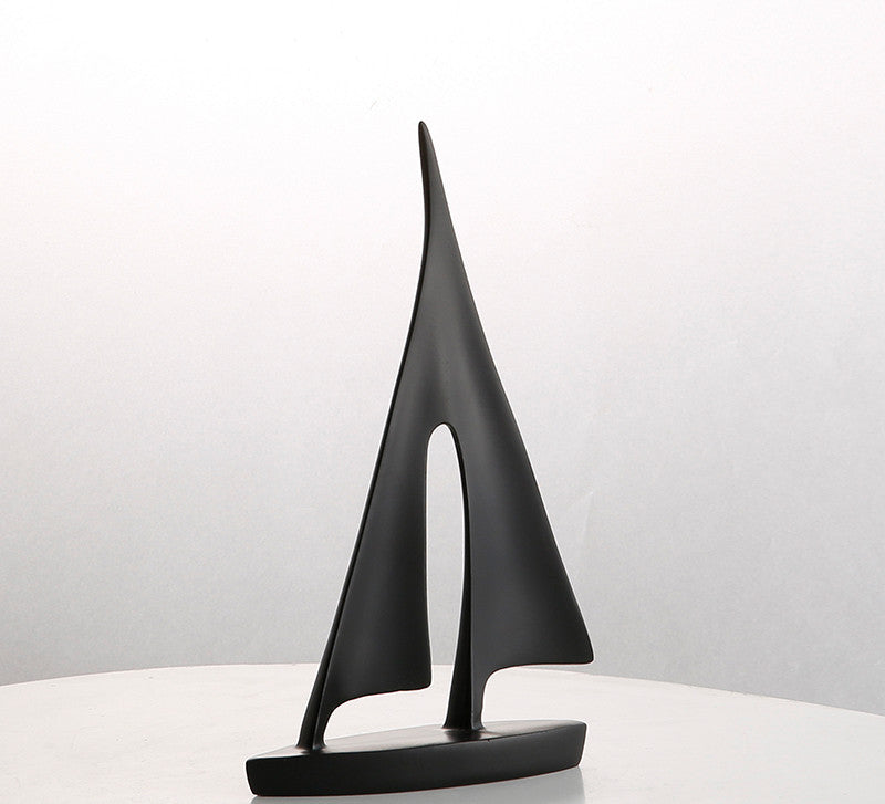 Black sailboat sculpture on a white surface with a light gray background