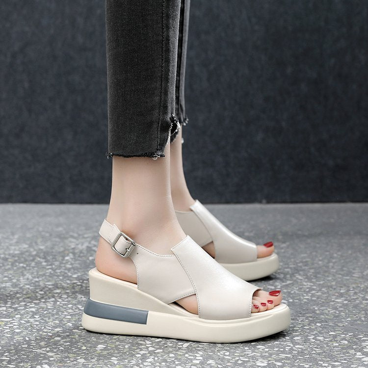White wedge sandals worn with dark jeans on a gray floor.