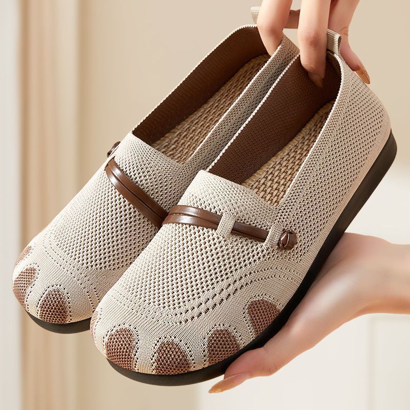 Pair of beige loafers with brown accents held by a person against a neutral background
