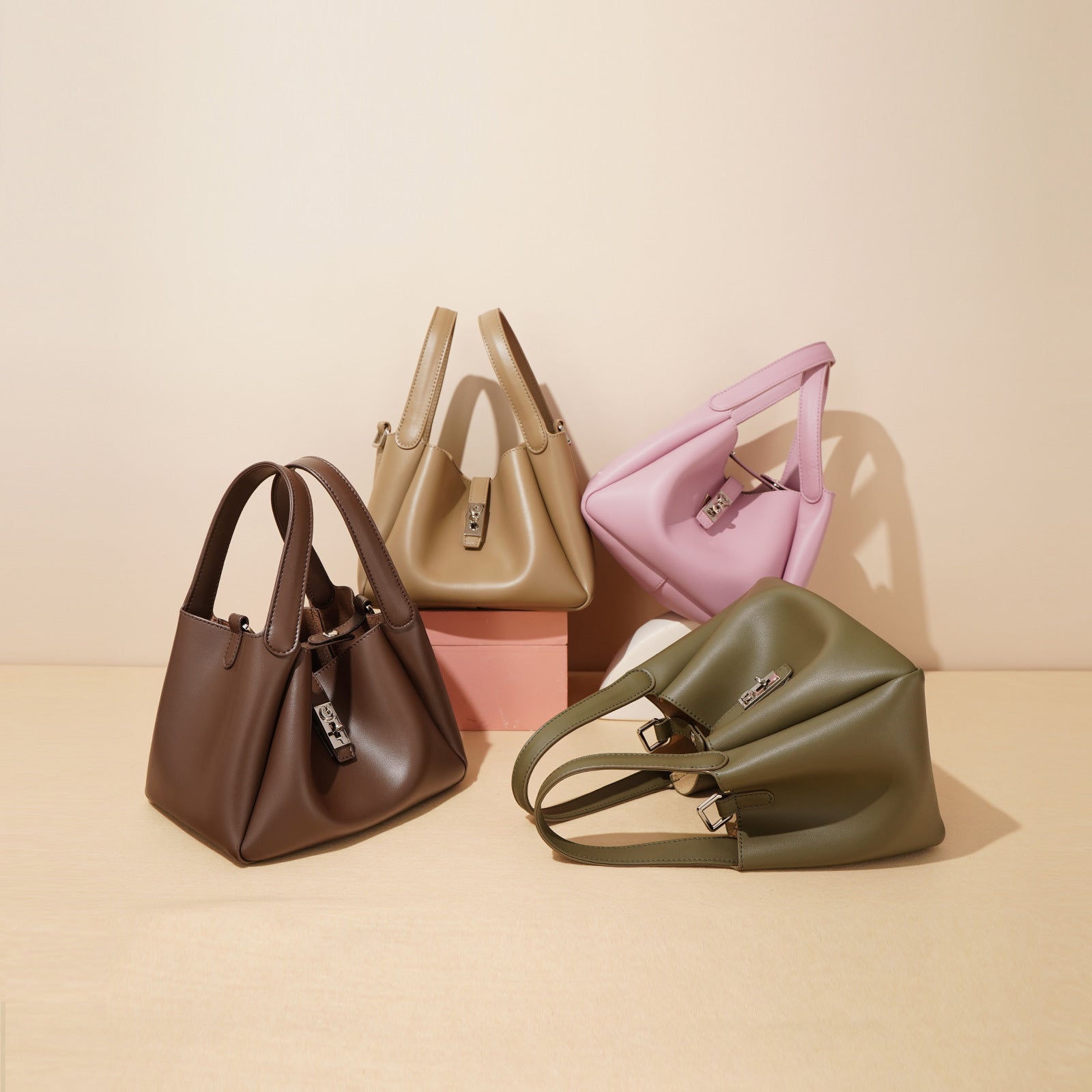 Five handbags in different colors arranged on a beige surface with a light pink background