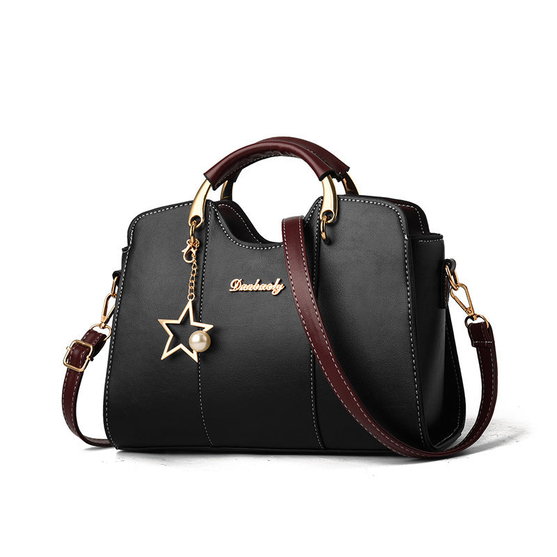 Black handbag with brown accents and a star charm on a white background