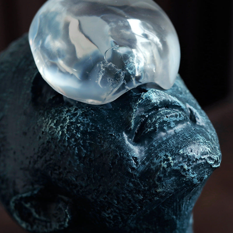 Close-up of a textured blue sculpture with a clear glass orb on top against a dark background