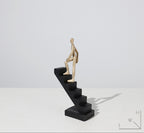 Statue of a figure climbing stairs on a white background