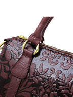 Close-up of a brown leather handbag with floral embossing and gold accents.