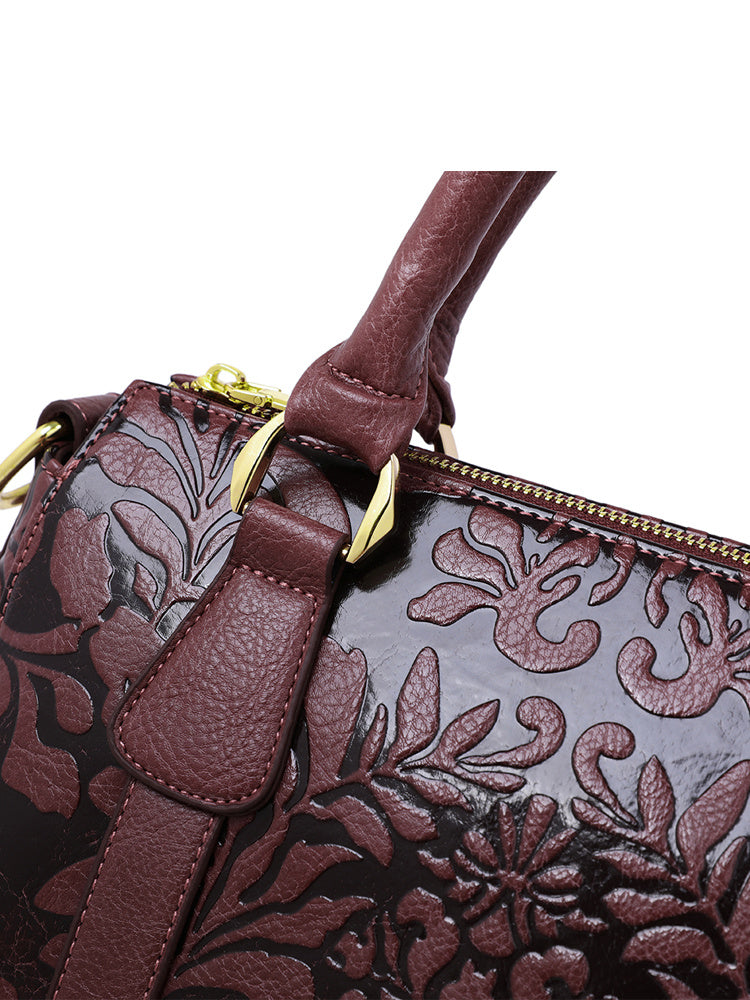 Close-up of a brown leather handbag with floral embossing and gold accents.