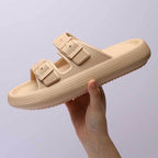 Beige sandal with buckle details held by a hand against a light purple background