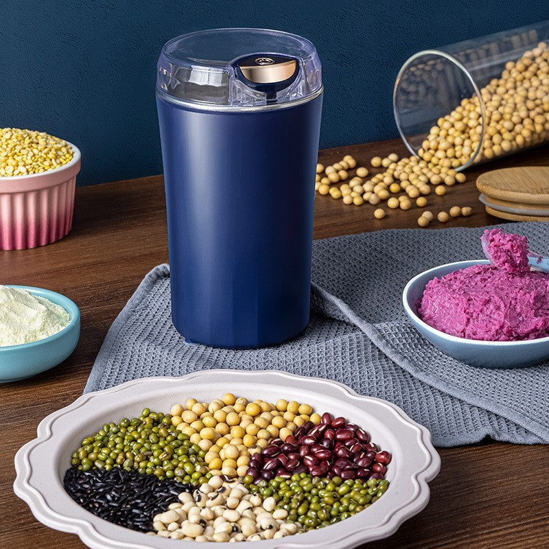 Navy blue spice grinder on a wooden table with various bowls of grains and a purple dish.
