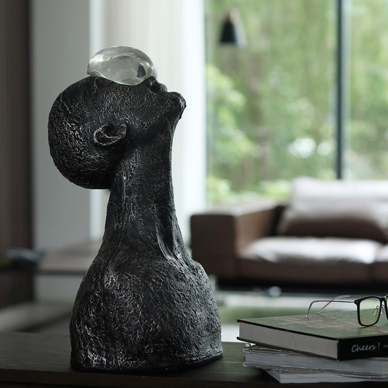 Decorative sculpture of a faceless figure with a crystal ball on a table in a living room.