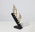 Decorative sculpture of three gold figures on a black base against a white background