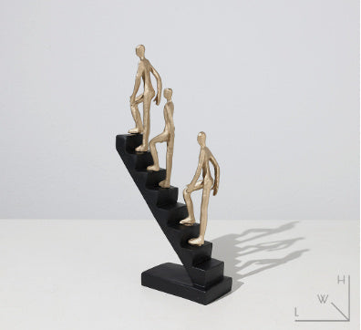 Decorative sculpture of three gold figures on a black base against a white background