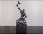 Bronze sculpture of a figure holding a hammer on a black platform with a light gray background