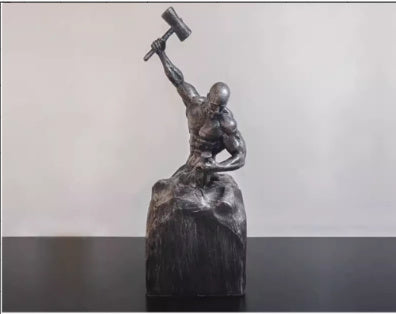 Bronze sculpture of a figure holding a hammer on a black platform with a light gray background
