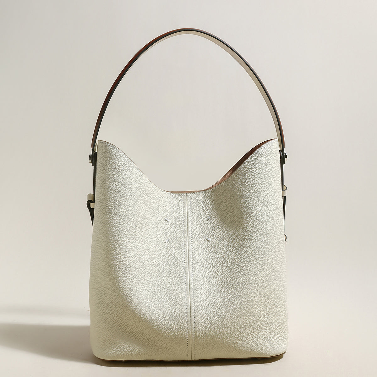 White leather handbag with brown handle on a light beige background